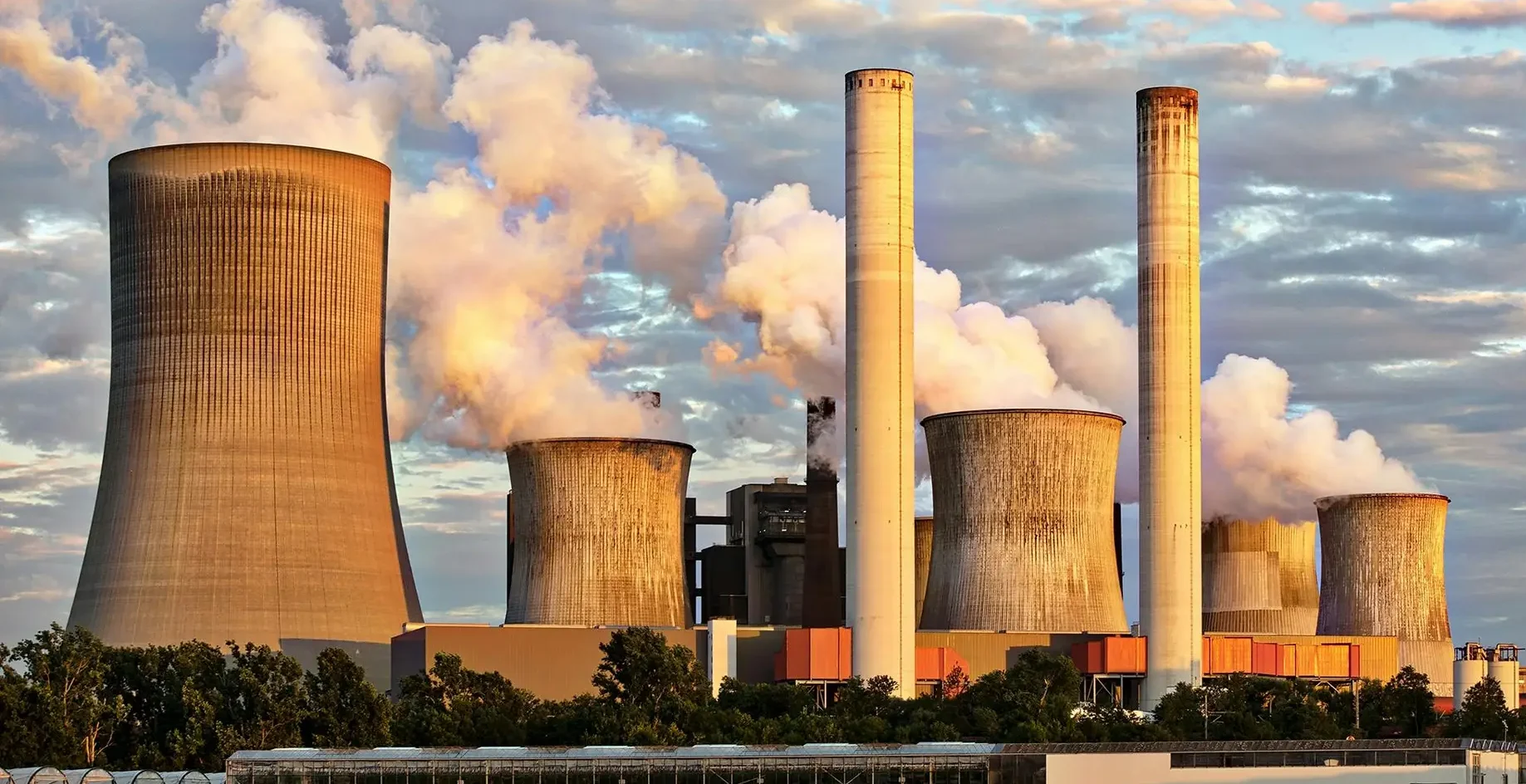 View of a power plant with smoke emissions under a cloudy sky, depicting industrial energy production.